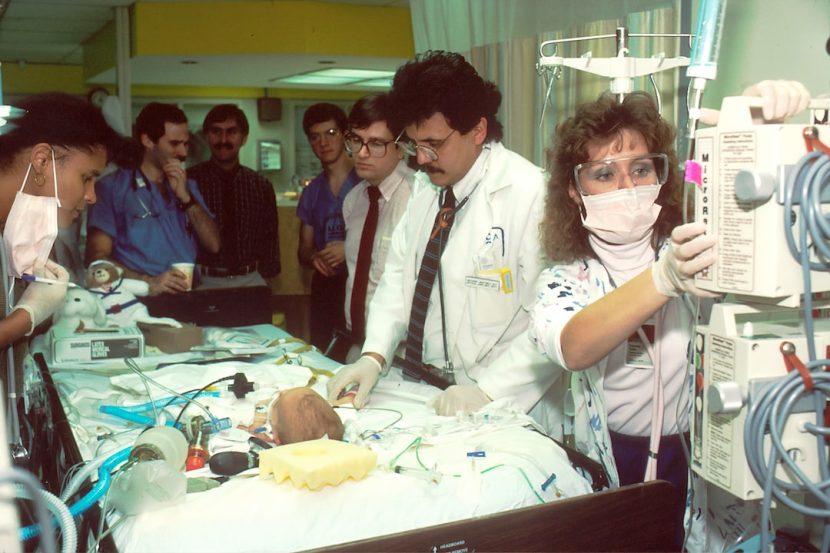 An image showcasing a sterile operating room, where a team of skilled surgeons is carefully transplanting a small heart into a child's delicate chest, surrounded by monitors, machines, and bright surgical lights